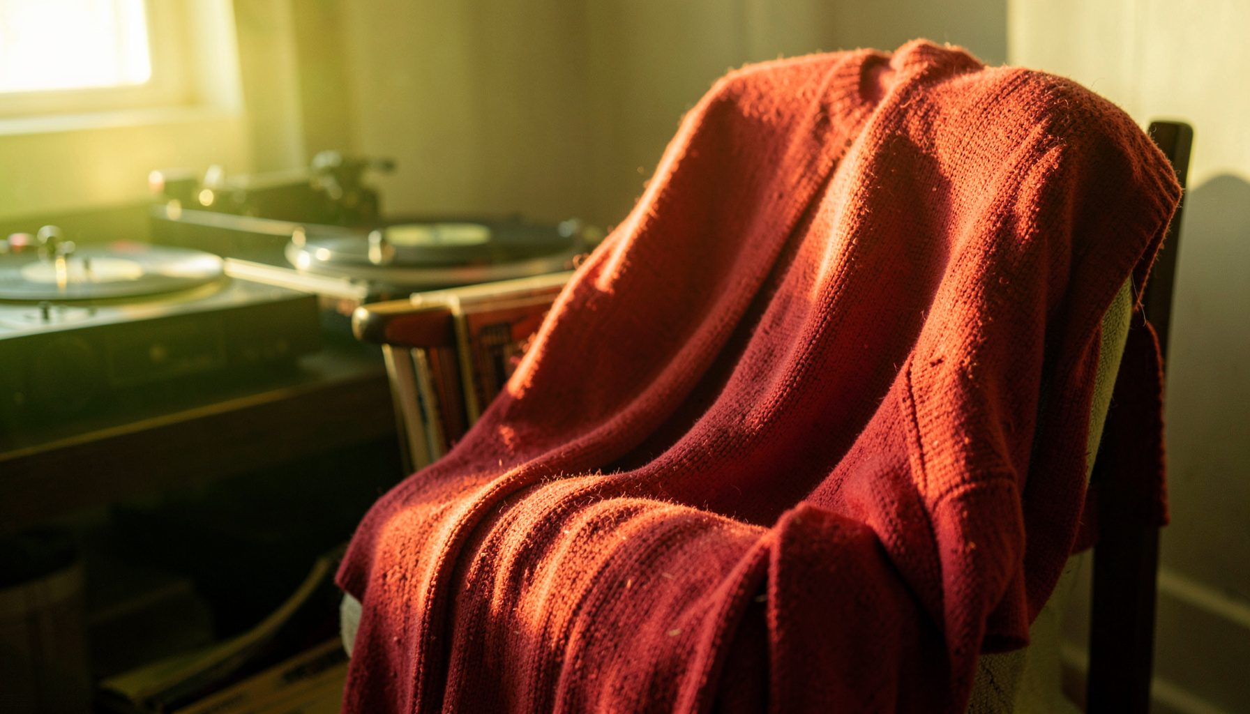 A soft knit pullover in cherry red draped over a chair, with a record player and vinyl records visible in the background.