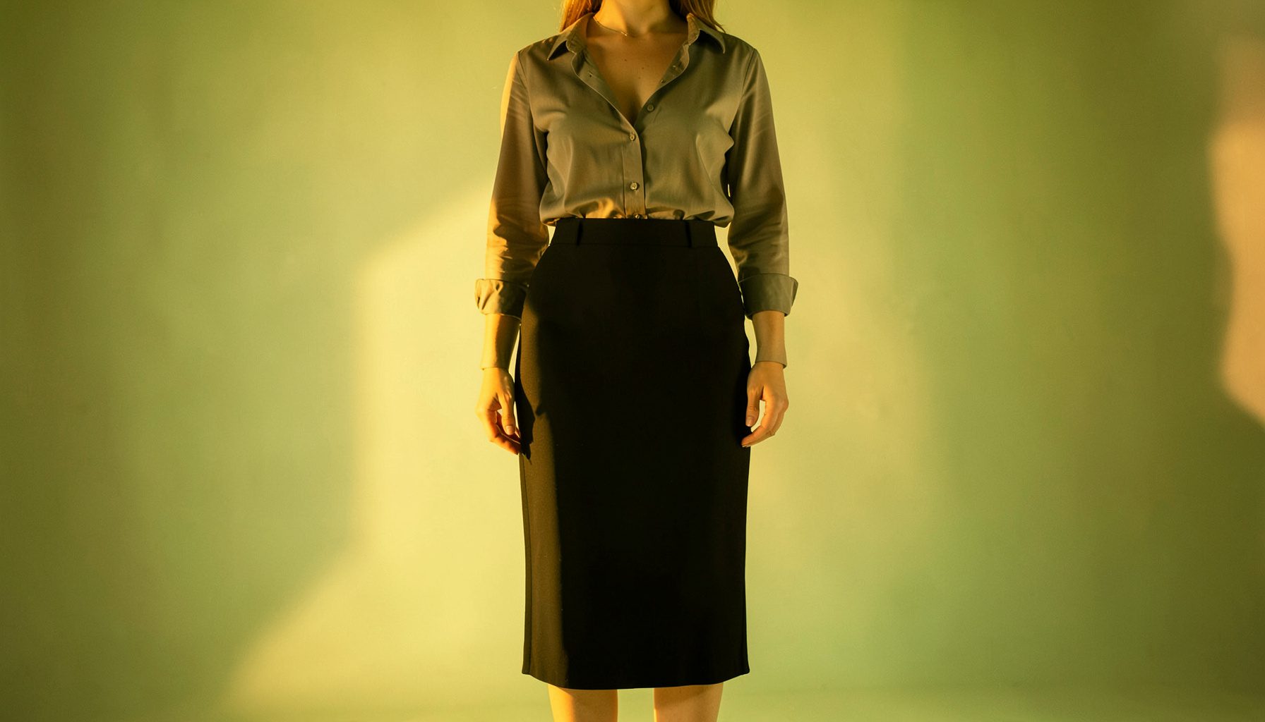 A high-waisted pencil skirt in black with a side slit, styled with a tucked-in blouse, in warm studio lighting.